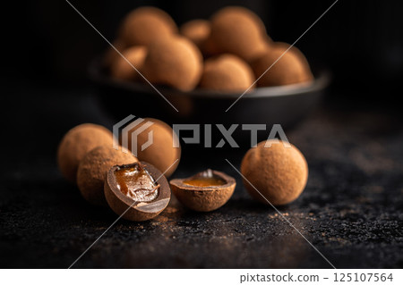Chocolate truffles with cocoa powder and caramel filling on black table. 125107564