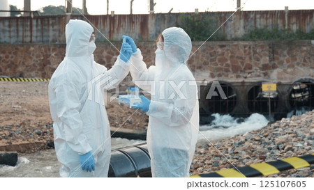 Ecologist sampling water from the river with test tube, Scientist or Biologist in a protective suit and protect mask collects sample of waste water from industrial for analyze, problem environment 125107605