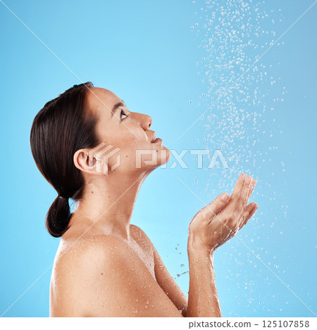 Water, shower and woman washing in a studio for body care, hygiene and to stop germs or bacteria. Health, wellness and Asian model cleaning her skin with aqua while isolated by a blue background. 125107858