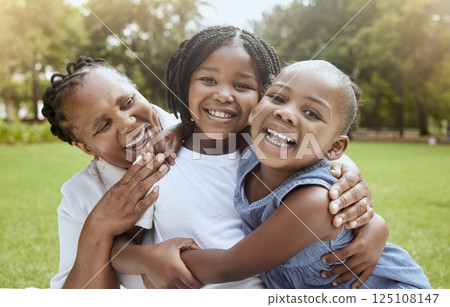 Love, black family hug and grandmother with children enjoy outdoor quality time together, peace or nature park freedom. Fun kids, bond and portrait of excited sisters play with grandma on grass field 125108147