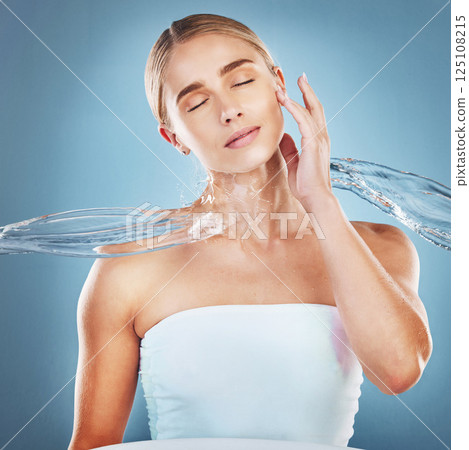 Beauty, skincare and woman with a splash of water for a natural facial routine in studio. Hygiene, cosmetic and healthy young model with clean face or skin treatment while isolated by blue background Beauty, skincare and woman with a splash of water for a natural facial routine in studio. Hygiene, cosmetic and healthy young model with clean face or skin treatment while isolated by blue background 125108215