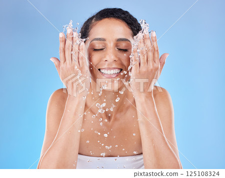 Skincare, water and woman washing face for clean, healthy and natural wellness against a blue studio background. Beauty, cleaning and happy model with splash for facial satisfaction and routine 125108324
