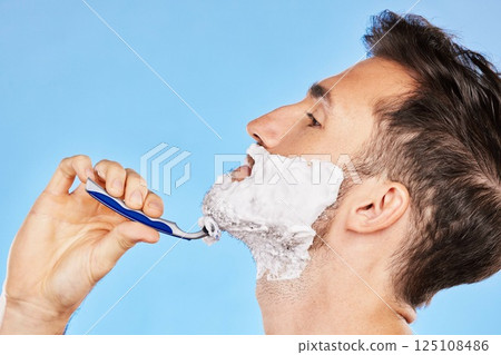 Shave, cream and man grooming his beard with a shaver in studio for health, skincare and hygiene. Foam, razor and model shaving his facial hair for a face or skin routine isolated by blue background. 125108486