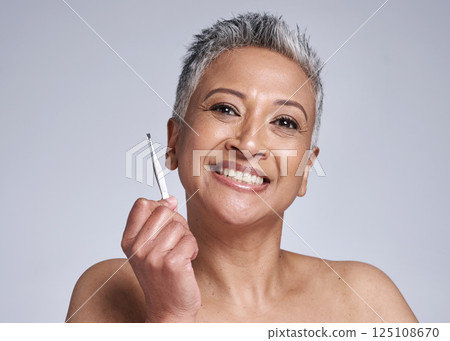 Beauty, tweezer and portrait of a senior woman grooming her facial hair for skincare in a studio. Cosmetic, self care and happy elderly lady with a smile for clear skin isolated by a gray background. 125108670