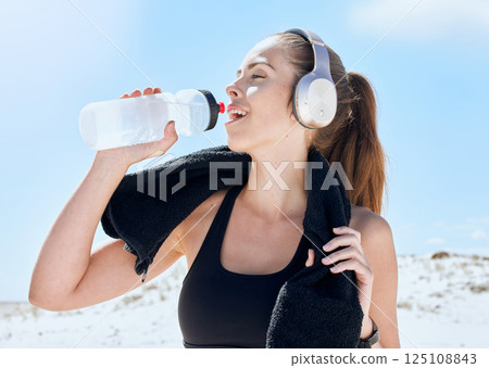Beach, workout and drinking water with headphones music for exercise, fitness and training break. Wellness, relax and sport woman streaming audio and resting body after cardio with water hydration. Beach, workout and drinking water with headphones music for exercise, fitness and training break. Wellness, relax and sport woman streaming audio and resting body after cardio with water hydration. 125108843
