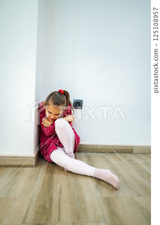 Little girl seeking comfort in a corner, finding solace on a calm afternoon while wearing a vibrant dress and thoughtful expression 125108957