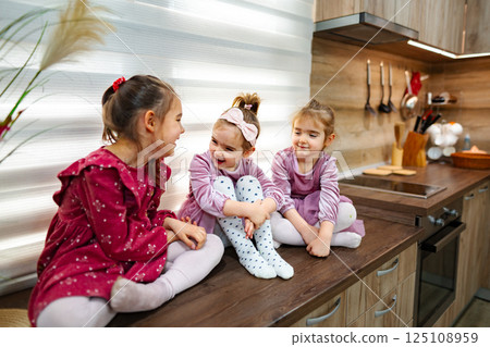 Delightful moments shared among three sisters in a cozy, bright kitchen during a sunny afternoon Delightful moments shared among three sisters in a cozy, bright kitchen during a sunny afternoon 125108959