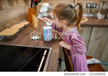 Young girl enjoying a sweet treat in a cozy kitchen during a sunny afternoon Young girl enjoying a sweet treat in a cozy kitchen during a sunny afternoon 125108980