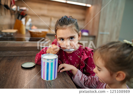 Two joyful children enjoy sweet moments in a cozy kitchen while sharing a delightful treat from a colorful container Two joyful children enjoy sweet moments in a cozy kitchen while sharing a delightful treat from a colorful container 125108989