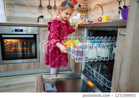 Young child helping with household chores in a spacious kitchen while loading the dishwasher with colorful dishes Young child helping with household chores in a spacious kitchen while loading the dishwasher with colorful dishes 125109003
