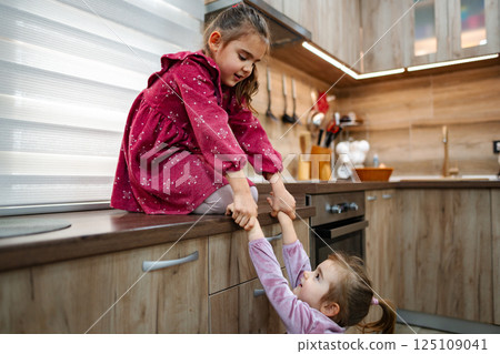 Two young sisters share a playful moment in a modern kitchen filled with warmth and creativity during a sunny afternoon 125109041