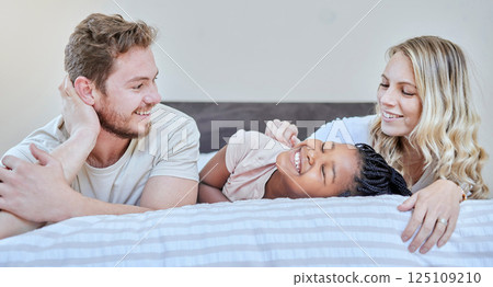 Family, adoption and love with happy, smile and care together on bed, relax and fun on weekend in home. Diversity, bedroom and happiness with bonding, support and relaxing with moth, father and girl 125109210
