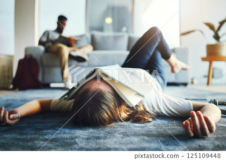 Burnout, student and tired woman with book on her face for knowledge exhaustion and fatigue. College, university and problem with a female lying on the floor covered in a notebook for studying 125109448