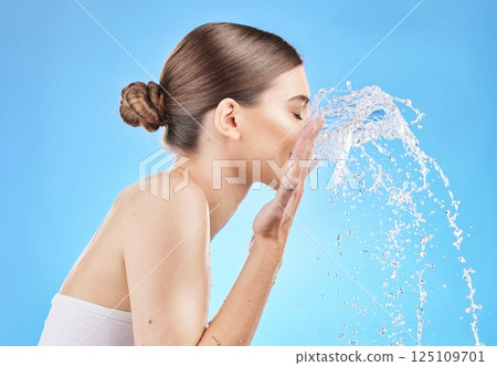 Skincare, water and woman cleaning face in studio on blue background for wellness, hygiene and facial cleanse. Beauty, hydration and girl washing skincare products, cosmetics and makeup with splash 125109701