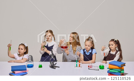 Science teacher and four girls conduct chemistry experiment with flasks and microscope in bright classroom. Science teacher and four girls conduct chemistry experiment with flasks and microscope in bright classroom. 125110526