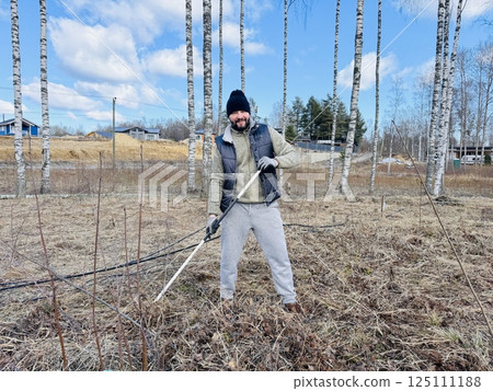a man raking dry grass in spring at his country plot a man raking dry grass in spring at his country plot 125111188