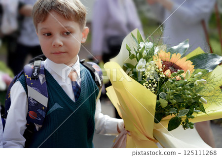 A 7-year-old boy carries a bouquet of flowers as he walks to his first day of school on September 1st, dressed in formal attire with a backpack. A 7-year-old boy carries a bouquet of flowers as he walks to his first day of school on September 1st, dressed in formal attire with a backpack. 125111268