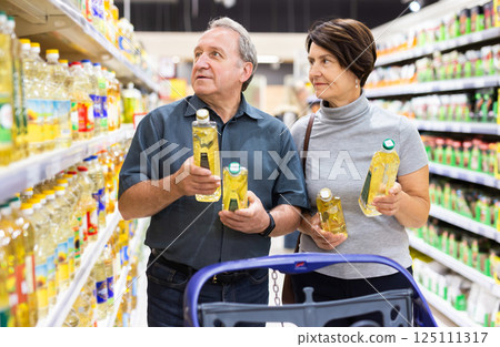 Elderly married couple choosing sunflower oil together in the grocery department of supermarket 125111317