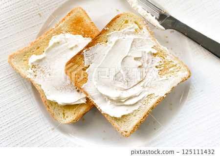 Cream cheese toast with a knife on a white plate. 125111432