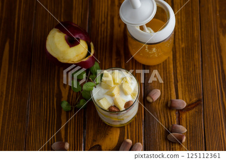 sweet homemade yogurt in a glass with apples, nuts and honey 125112361