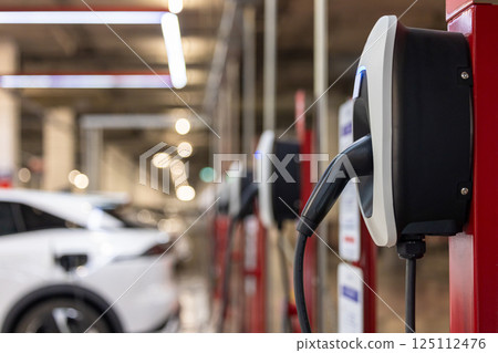 EV charging station and electric car, Electric car charging station for charge EV battery, Plug for vehicle with electric engine, EV charger clean energy, Charging point at car parking lot. 125112476