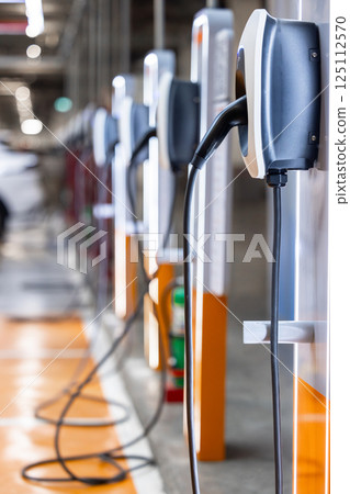 EV charging station and electric car, Electric car charging station for charge EV battery, Plug for vehicle with electric engine, EV charger clean energy, Charging point at car parking lot. 125112570