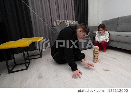 Two players engaged in a strategic game of tower blocks in a cozy living room, showcasing focus and anticipation on a winter evening Two players engaged in a strategic game of tower blocks in a cozy living room, showcasing focus and anticipation on a winter evening 125112600
