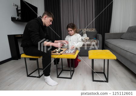 Young boy and girl engaged in chess match indoors during cozy evening hours filled with laughter and friendly competition at home 125112601