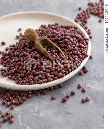 Plate full of dried red azuki beans with a wooden scoop closeup. East Asian legumes, vegetarian food 125112646