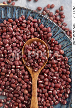 Blue plate full of dried red azuki beans with a wooden spoon top view. Vegetarian protein source 125112649