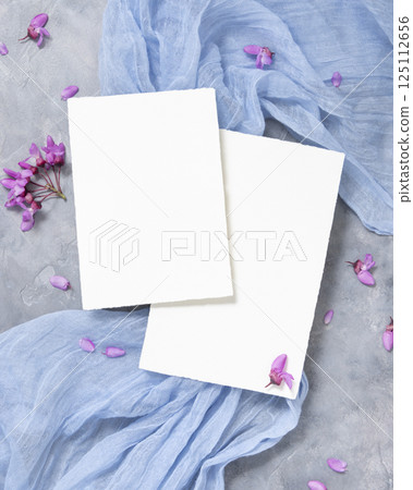 Vertical blank cards on fabric near wild purple flowers top view on gray, spring wedding mockup Vertical blank cards on fabric near wild purple flowers top view on gray, spring wedding mockup 125112656