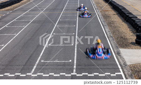 Motion blur kart driver crossing the start and finish line on kart race track circuit, Go kart racer crossing the start and finish line, Extreme sport competition winner. Motion blur kart driver crossing the start and finish line on kart race track circuit, Go kart racer crossing the start and finish line, Extreme sport competition winner. 125112739