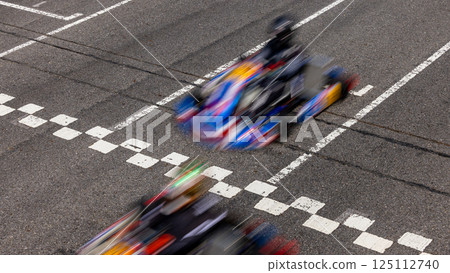 Motion blur kart driver crossing the start and finish line on kart race track circuit, Go kart racer crossing the start and finish line, Extreme sport competition winner. Motion blur kart driver crossing the start and finish line on kart race track circuit, Go kart racer crossing the start and finish line, Extreme sport competition winner. 125112740