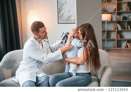 Using stethoscope. Male doctor is taking care of woman's newborn baby indoors Using stethoscope. Male doctor is taking care of woman's newborn baby indoors 125113043