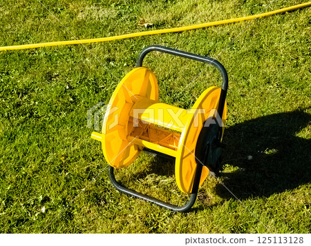 Empty yellow hose reel on green grass. Proper storage of garden hoses 125113128