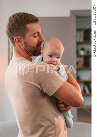 Holding kid in hands. Father with his newborn baby is indoors. Conception of single dad 125113207