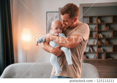 Holding kid in hands. Father with his newborn baby is indoors. Conception of single dad 125113211