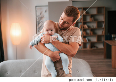 Holding kid in hands. Father with his newborn baby is indoors. Conception of single dad Holding kid in hands. Father with his newborn baby is indoors. Conception of single dad 125113214