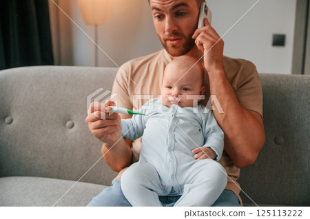 Sitting and talking by phone. Father with his newborn baby is indoors. Conception of single dad 125113222