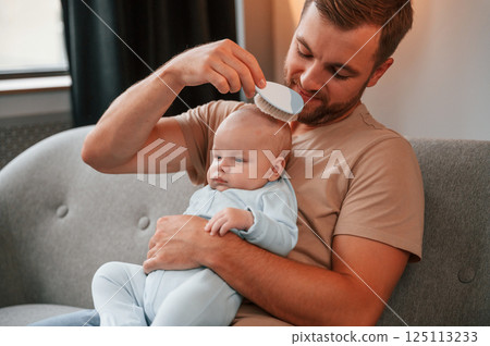 Brushes the head. Father with his newborn baby is indoors. Conception of single dad 125113233