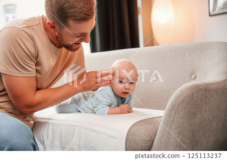 Newborn baby is laying down on the sofa. Man is indoors. Conception of single dad 125113237