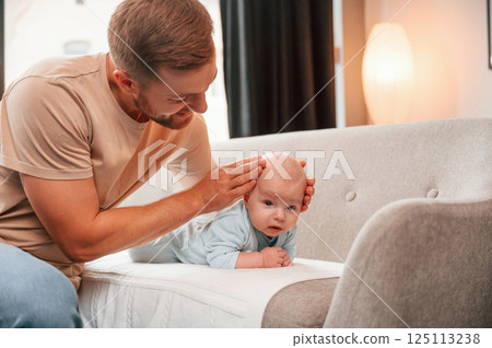 Newborn baby is laying down on the sofa. Man is indoors. Conception of single dad Newborn baby is laying down on the sofa. Man is indoors. Conception of single dad 125113238