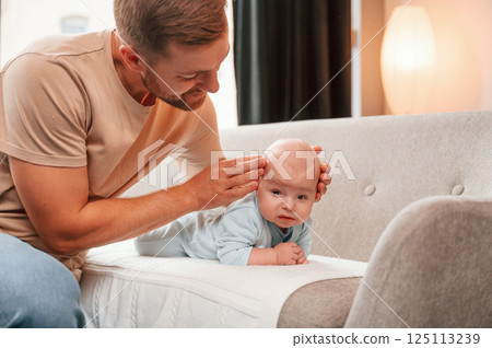 Newborn baby is laying down on the sofa. Man is indoors. Conception of single dad 125113239