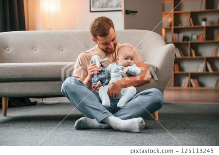 Playing by using soft toy. Father with his newborn baby is indoors. Conception of single dad Playing by using soft toy. Father with his newborn baby is indoors. Conception of single dad 125113245