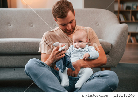 Playing by using soft toy. Father with his newborn baby is indoors. Conception of single dad Playing by using soft toy. Father with his newborn baby is indoors. Conception of single dad 125113246