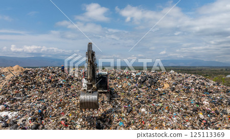 Bulldozer working on massive lanfill waste site with mountain background, Heavy machinery manage plastic waste at larg garbage dump, Excavtor at landfill global waste crisis concept. Bulldozer working on massive lanfill waste site with mountain background, Heavy machinery manage plastic waste at larg garbage dump, Excavtor at landfill global waste crisis concept. 125113369
