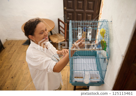 Smiling Woman Feeding Budgies in a Cage at Home 125113461