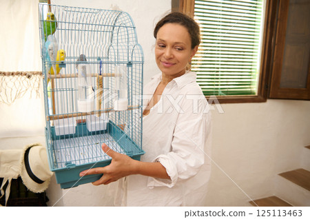 Woman Smiling While Holding a Birdcage with Colorful Parakeets Woman Smiling While Holding a Birdcage with Colorful Parakeets 125113463