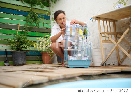Woman Tending to Pet Budgerigar Cage in Outdoor Garden Scene Woman Tending to Pet Budgerigar Cage in Outdoor Garden Scene 125113472