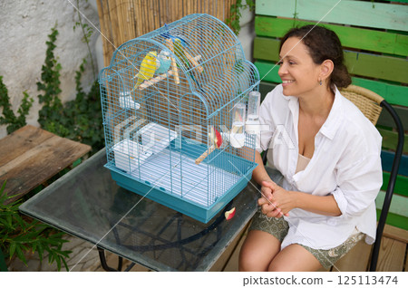 Woman Smiling at Birds in Cage Outdoors on a Sunny Day 125113474